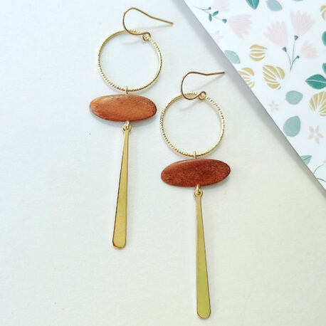 Boucles d'oreilles inspiré du symbole égyptien d'Ânkh. Ce sont des boucles pendantes. sous le crochet d'oreille il ya un cercle de 15mm délicatement strié, en dessous une pièce en bois en forme de planche de surf horizontal puis en dessous une languette plate dorée. l'ensemnle mesure 7cm