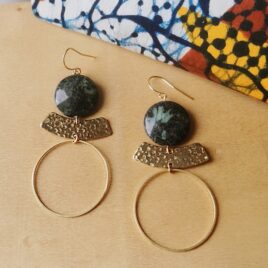 Boucles d'oreilles pendantes et longues composées de 3 éléments. le premier, en dessous du crochet d'oreille doré est une perle ronde et plate de 2cm de jaspe kambaba, puis un élément plat dore forme bateau martelé, en dessous est suspendu un cercle doré de 4cm